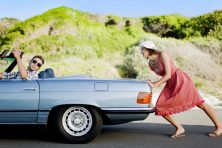 A man steers the car as a woman pushes it up a hill.