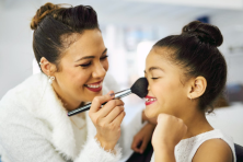 A mother puts makeup on her daughter's face as they play dress up.