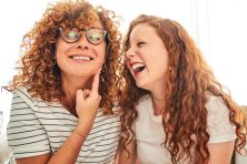 A mother puts her finger to her cheek to imply her teenage daughter to give her a kiss on the cheek.