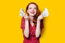 A woman flaunts money against a yellow background.