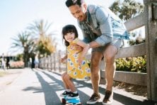 A father teaches his daughter how to ride a skateboard.
