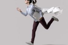 A business woman runs with papers falling behind her.