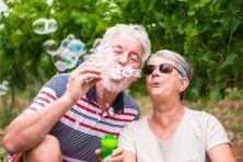 A retired couple blow bubbles into the air while relaxing outside.