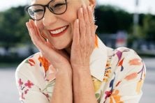 A retired woman wearing glasses smiles.