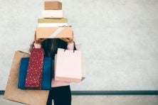 A woman holds numerous shopping bags and gift boxes to show excessive spending.