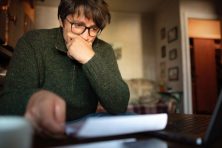 A man looks stressed as he looks at debt next to his laptop.