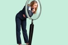 A business woman looks through a magnifying glass.