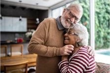 A couple laugh and snuggle while standing up in their house.