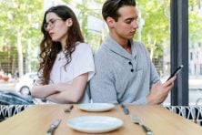 A couple look unhappy on a date with the boyfriend distracted by a text message.