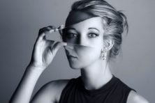 A woman holds up a mirror to her face to show her eyes and nose off center. This is meant to represent a woman battling with something such as gaslighting.