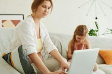 Single parent reviewing their family budget on a laptop while managing household tasks