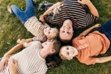 A family of four lay in the grass together while smiling.