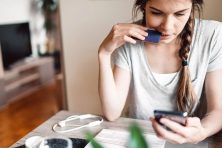 A young woman looks at her phone while holding a credit card.