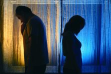 An unhappy married couple stand with their backs toward each other.