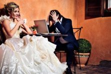 A bride sips coffee as her husband looks stressed out over the wedding bill on his laptop.