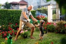 A man dances in the garden with his dog.