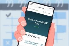 An illustration shows a hand holding up a cell phone displaying the FASFA website.