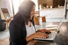 A woman laughs as she types on a laptop. Amazon product reviewers evaluate items and write reviews online.