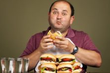 A man eats a plate full of burgers.