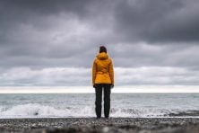 A woman overlooks storm clouds at the beach while wearing a yellow jacket.
