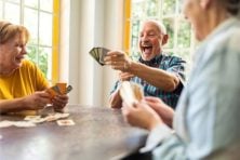 A group of three friends play a card game. A guy reacts to having a winning hand at the card game.