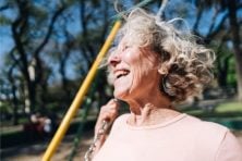 A retired woman swings on a swing at a park with the wind blowing through her hair.