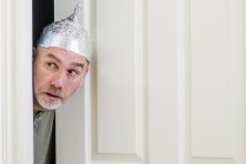 A man peeps his head out of a doorway while wearing aluminum foil over his head.