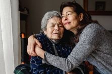 A daughter hugs her elderly mother who is in a wheelchair.