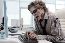 A zombie types on a computer in an office.