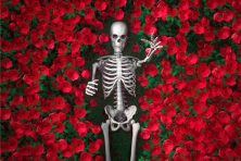 A skeleton reaches through a bush of roses.