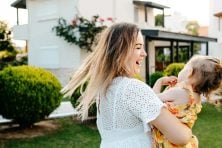 A mother spins her daughter around in their front yard outside of their house.
