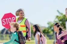 A crossing guard leads a group of children across of the street to attends school.
