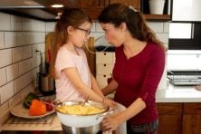 A mother and daughter share a piece of spaghetti as they prepare dinner.