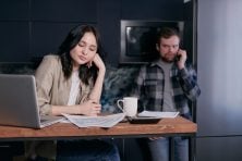 A woman stares at bills while a man talks on the phone next to her.