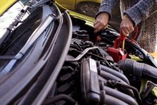 A woman uses jumper cables to start up a yellow Honda fit.