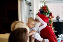 A man dressed a santa claus kisses his grandchild at home on Christmas.