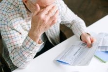 A senior citizen male looks stressed as he looks over his medical bills.