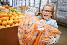 A girl carries a large bag of carrots.