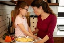 A mother and daughter share a piece of spaghetti as they prepare dinner.