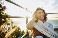 A woman laughs while sitting on a pier with the ocean in the background.