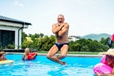 A retired age man jumps into the pool doing a canon ball.
