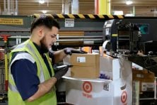 A man works in a Target distribution center. He is scanning a package.