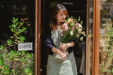 A woman leaves a florist shop with a bouquet in her arms.