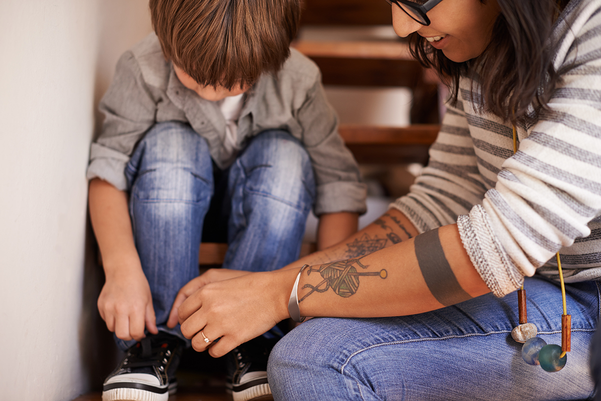 A mother helps her son get ready for school by tying his shoe.