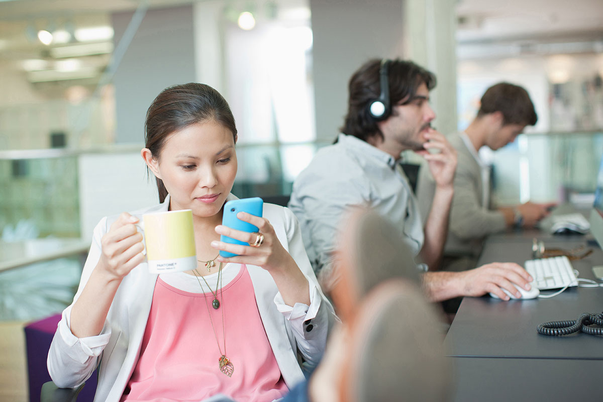 Businesswoman drinking coffee and looking at phone with feet up in office