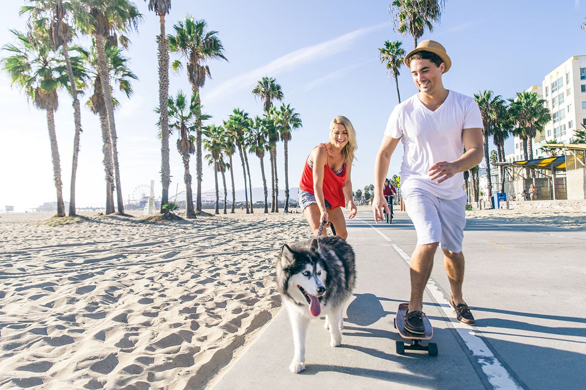 couple in california skating with dog by beach