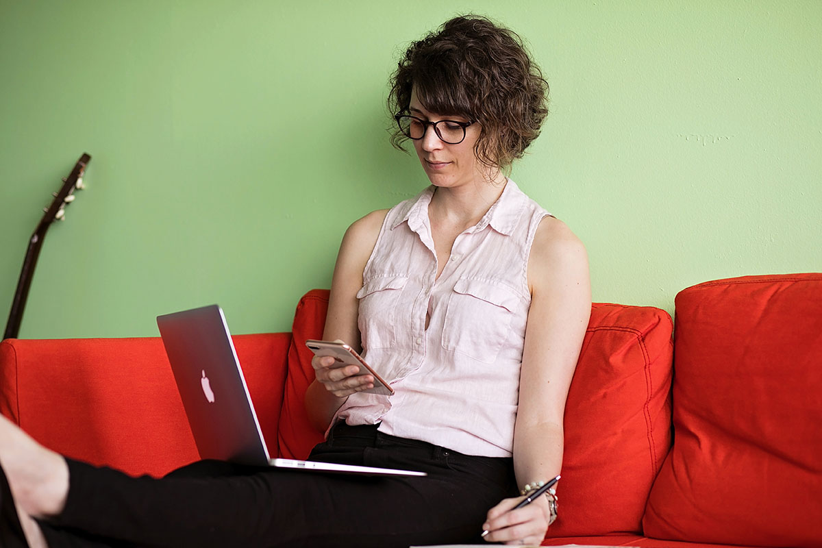 Dana Sitar sitting at home on the couch with phone and laptop