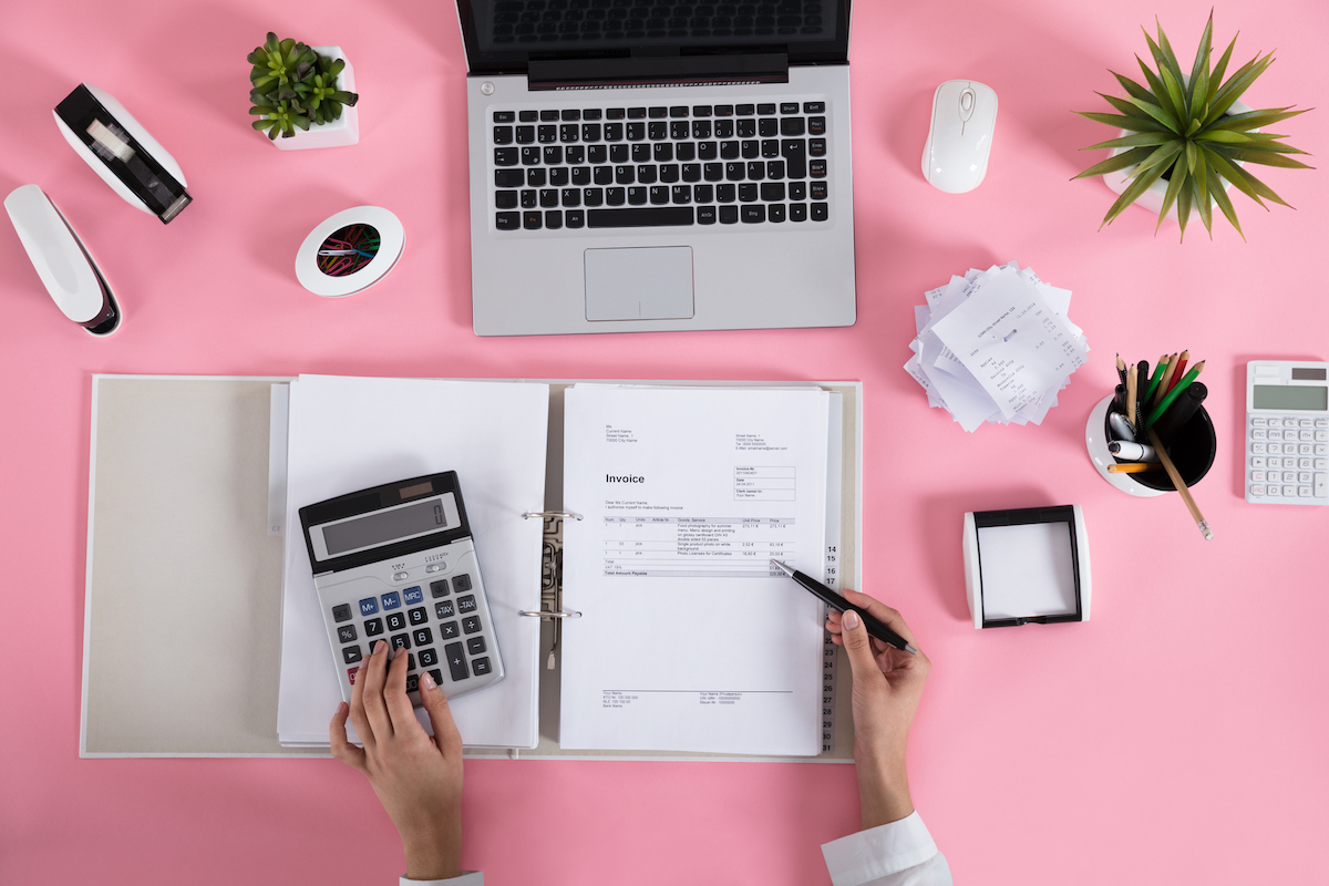 Elevated View Of A Businesswoman Calculating Invoice Using Calculator On Pink Desk