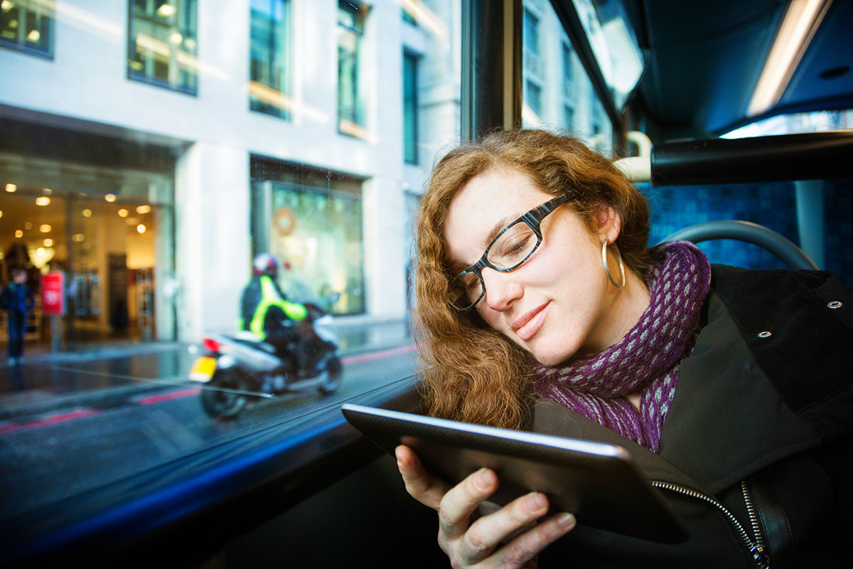 Young woman entertained by her tablet on a bus ride to work.