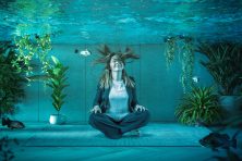 A business woman does yoga while sitting in an office underwater.